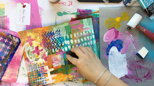 A hand stamping with a foam stamp in an art journal on a messy desk.