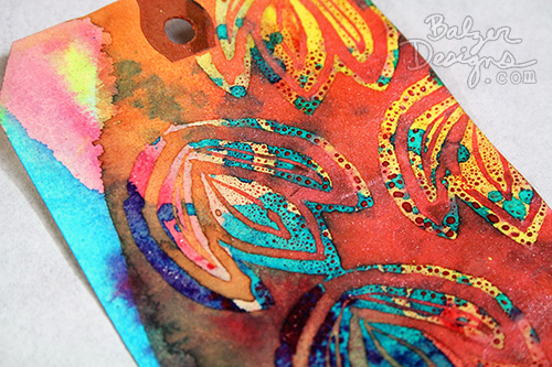 Close up of mixed media tag featuring stamped flowers.