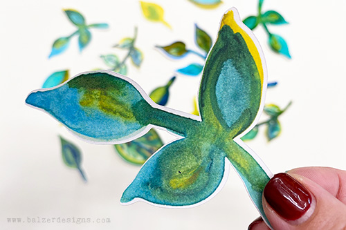 A watercolored leaf cut out and held by fingers.