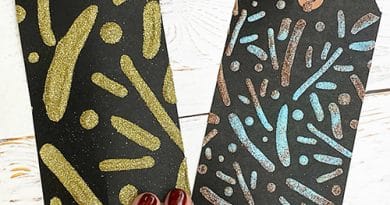 Two black tags with a stenciled design that has been heat embossed. There are four fingers (with red nails) laying on the tags.