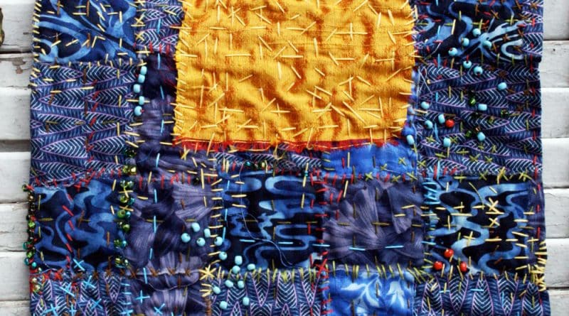 Small hand stitched quilt with a big yellow square in the middle and lots of stitching and beading.