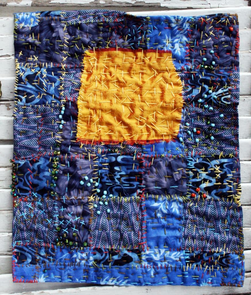 Small hand stitched quilt with a big yellow square in the middle and lots of stitching and beading.